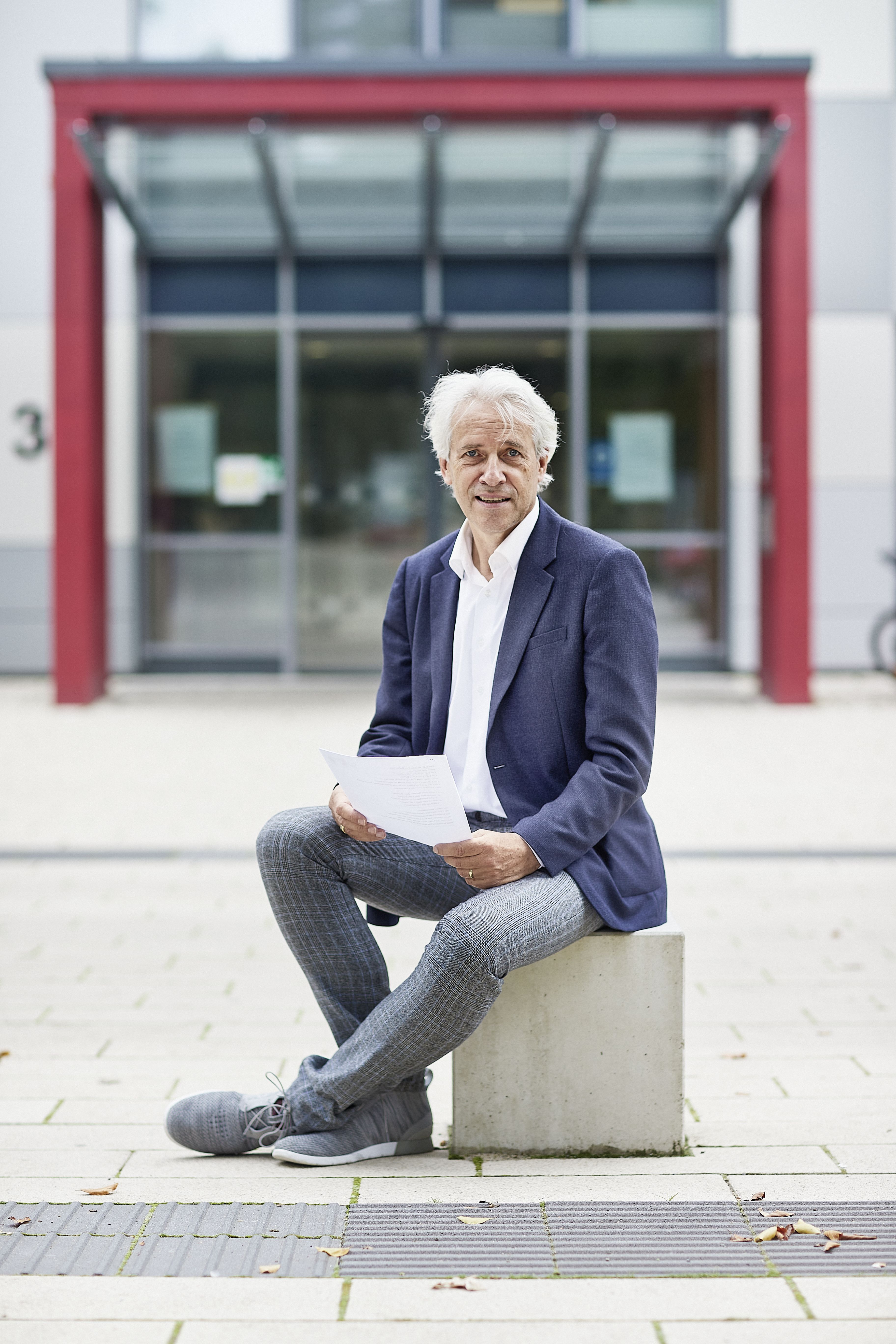 Prof. Dr. Meinolf Noeker sitzt vor dem Eingang einer LWL-Klinik