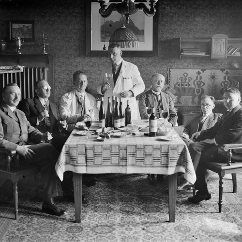 Schwarzweißfoto von einer Gruppe Männer, die mit Wein auf ein Ereignis anstoßen.
