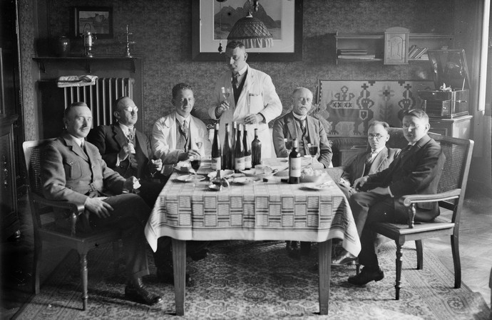 Schwarzweißfoto mit Männern an einem Tisch, die auf ein Ereignis anstoßen.