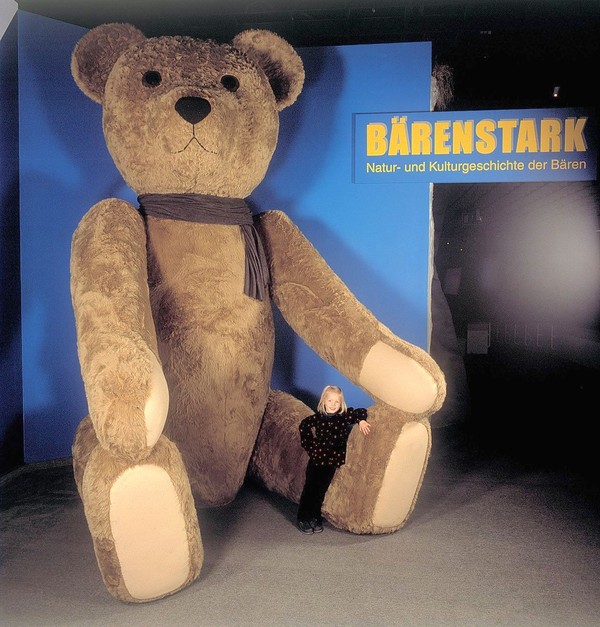 Übergroßer Teddy im LWL-Museum für Naturkunde mit jungem Mädchen, was am Bein des Teddys lehnt